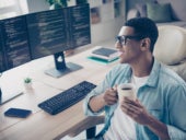 Photo of a happy clever geek guy enjoying his cup of coffee while working on coding inside his remote workspace.