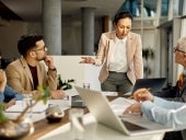 Asian female leader using laptop and communicating with her business team during meeting in the office.