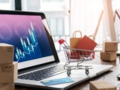 Shopping bags in shopping cart and credit card on laptop with paper boxes on table.